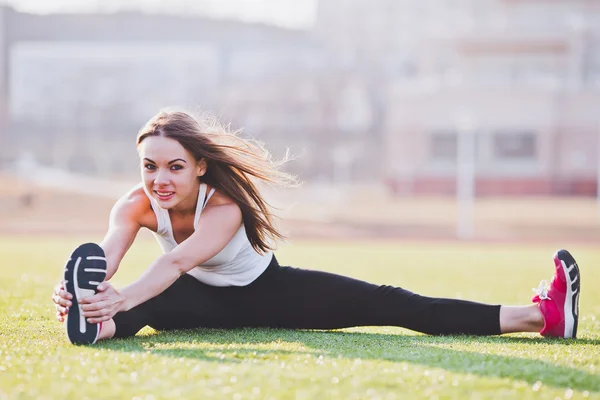 Young woman stretching her foot while performing splits on a field on a sunny summer day