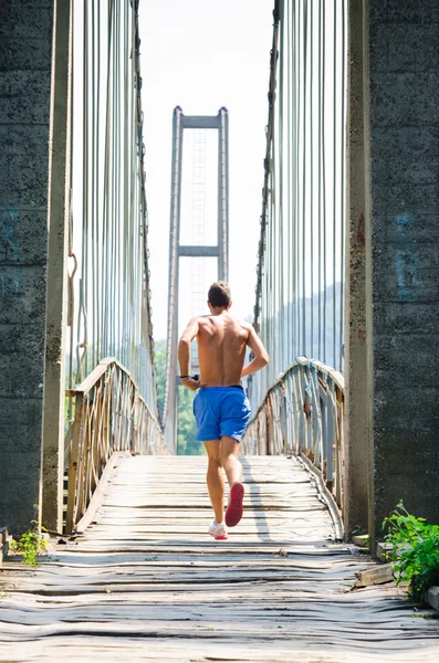 Morning time view of a man running along old suspension bridge.
