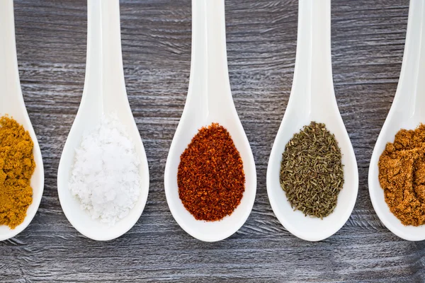 Five ceramic spoons lined up in a line filled with colorful spices