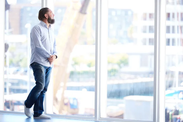 Full body shot of man with beard looking out window