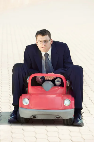 Disappointed Businessman Sitting in the Red Toy Car
