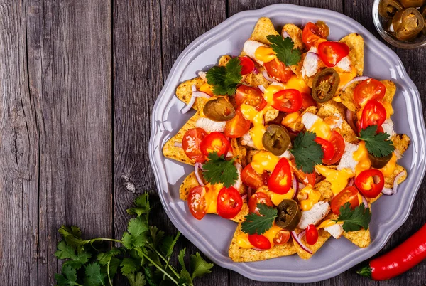 Nachos with melted cheese sauce, jalapeno, chicken, vegetable.