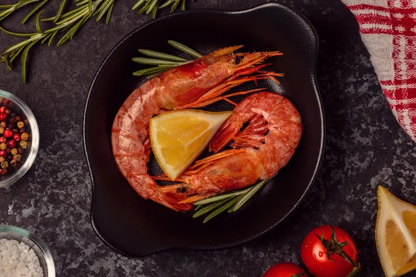 Grilled shrimps with lemon and rosemary on frying pan.