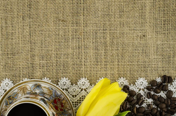 Frame of coffee cup, yellow flower and coffee beans on linen background