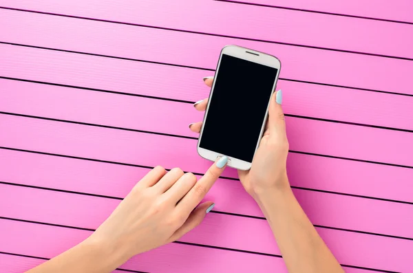 Female hand using white mobile phone over pink background