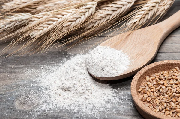 Flour in a wooden spoon and wheat grains