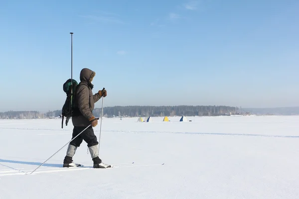 The man the traveler with a backpack skiing on snow of the river