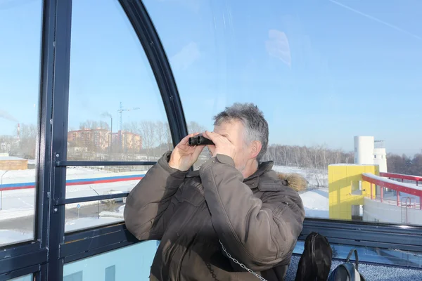 The man looking in binoculars from a ferris wheel  cabin