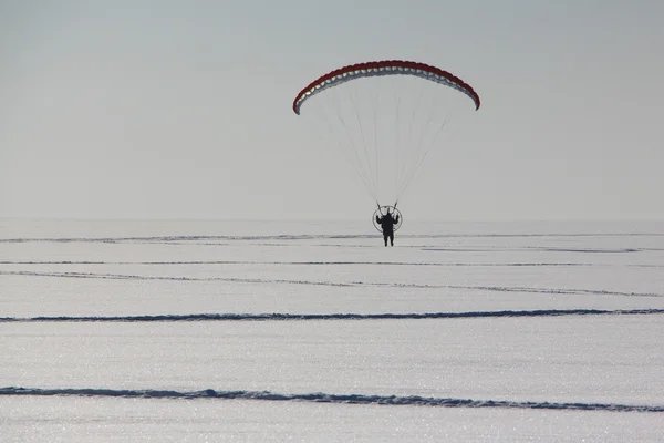 The person flying on a motorized paraplane against the snow