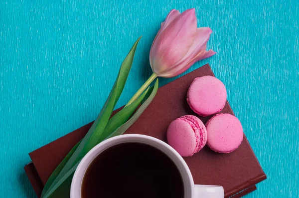 Pink tulip, a cup of coffee, books and three pink macaroons