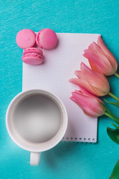 Three pink tulips, a cup of coffee and three pink macaroons