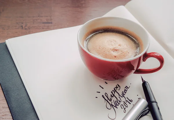 A cup of coffee resting on a book with text happy new year 2016.