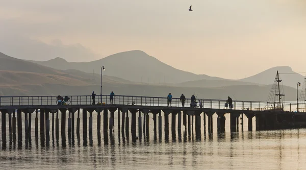 The silhouettes of the pier,boats,fishermen on the background of the mountains and Bay.