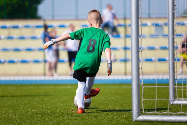 Young boy soccer football goalkeeper kicking soccer ball on a sports field.