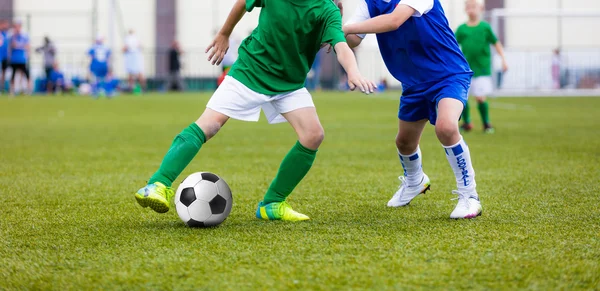 Young boys playing football soccer game on sports field. Running soccer players in sport shirts. Kids running and kicking soccer ball.