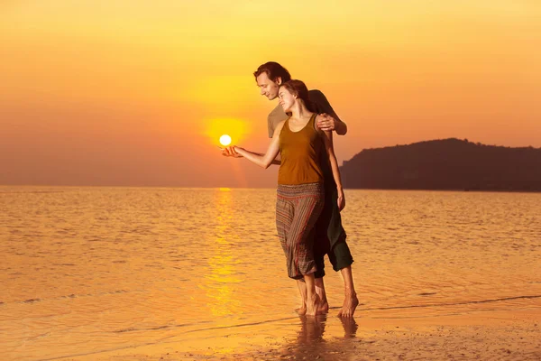 Beautiful young couple is touching sun at outdoors amazing golden sea sunset background.
