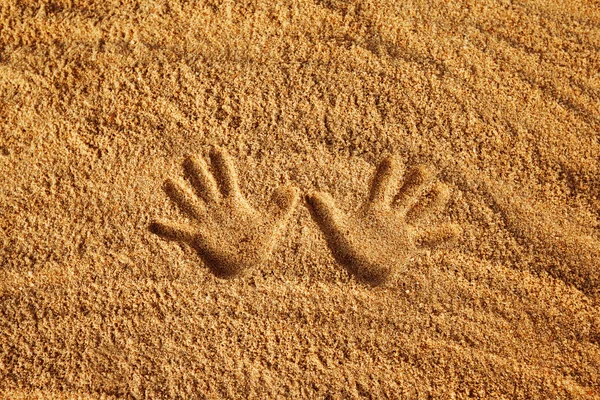 Close-up image of hand prints on yellow textured sand background