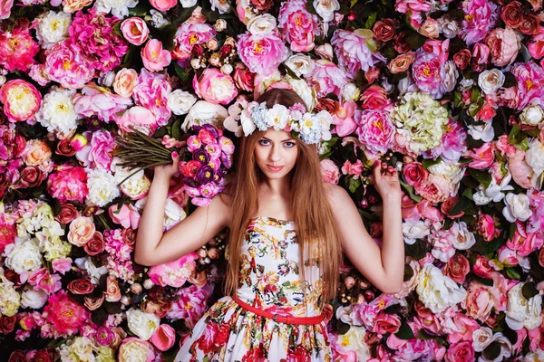 A beautiful young girl with flowers bouquet near a floral wall.