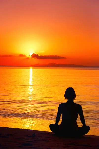 A silhouette of meditating woman at the sea shore at orange sun