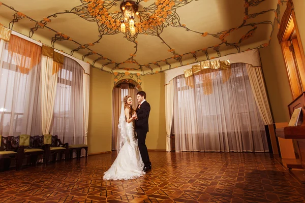 Wedding dance of a beautiful wedding couple in a stunning vintage spacious hall with wooden parquet and pattern ceiling.