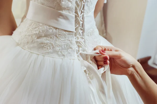 A closeup image of wedding preparations. Bridesmaid is helping put bride elegant luxury dress.
