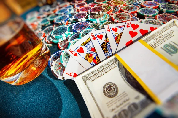 A poker table with chips, glass of wiskey, bundle of money and heart flash royal combination of playing cards.
