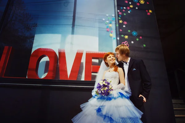 Happy wedding couple is laughing at street shop window with caption Love background.