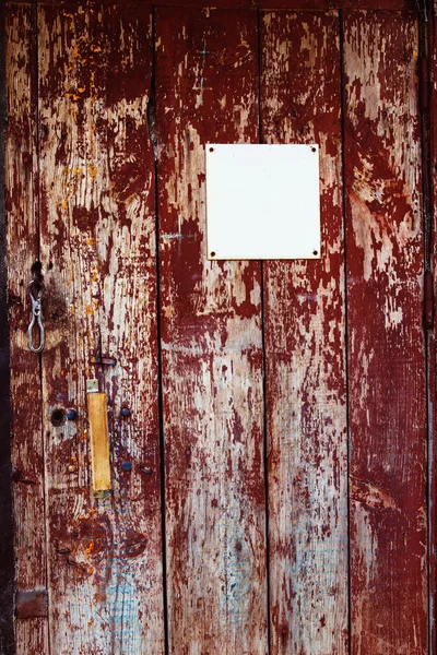 Closeup image of red wooden rusty door with white blank plate. Background for advertising.