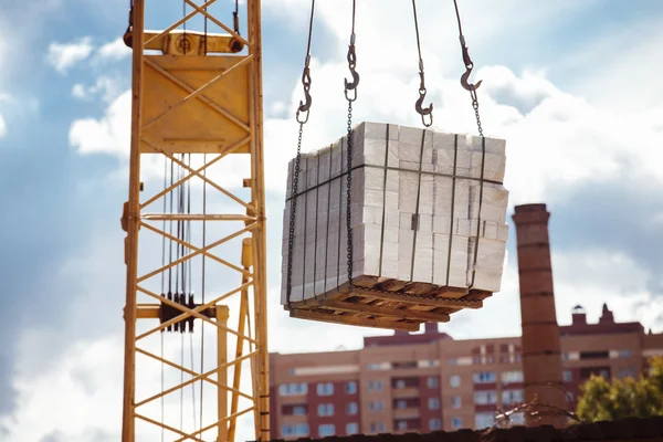 Closeup image of crane lifting heap of bricks at blue sky summer background.