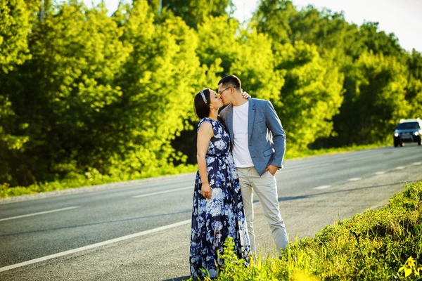Portrait of happy couple standing at road and kissing at natural green summer background.