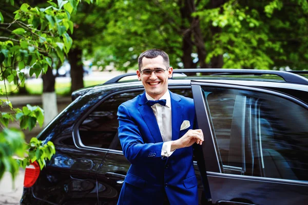 Portait of happy elegant man in suit and glasses holding car doo