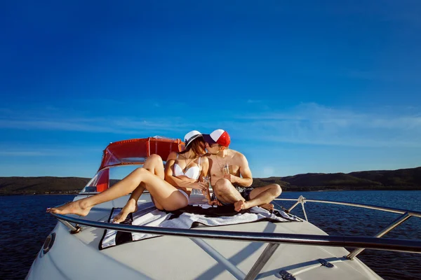 Beautiful young happy couple is sitting on boat and kissing at blue background.