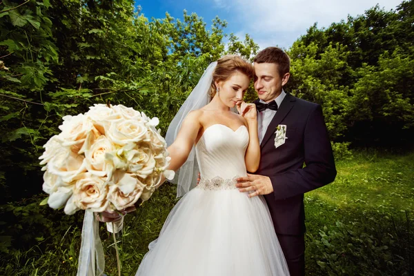 Closeup image of white roses wedding bouquet and laughing bride and groom at summer park background.