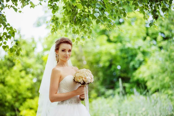 Closeup portrait of beautiful bride with flowers bouquet standing outdoors at green natural background.