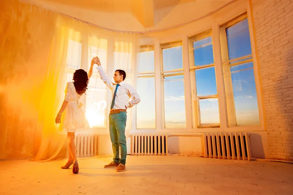 Beautiful young couple is dancing at yellow summer sunset window background.