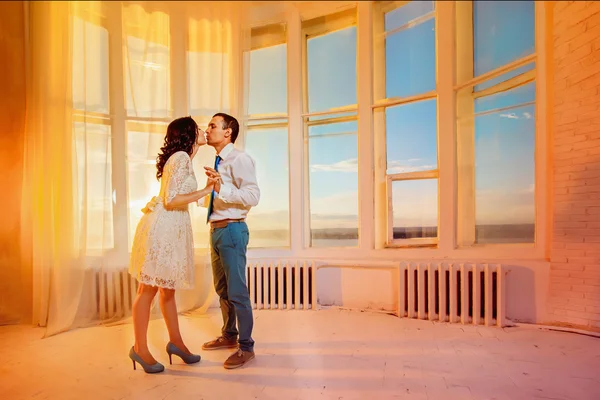 Beautiful young couple is kissing at yellow summer sunset window