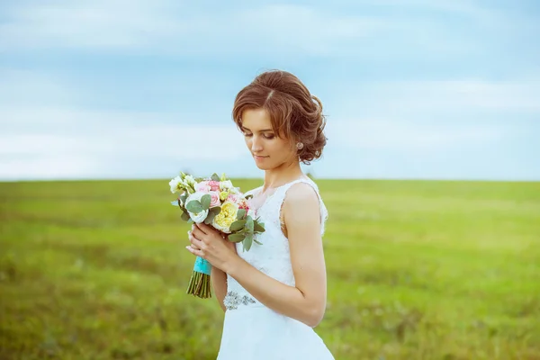 Closeup portrait of beautiful bride with wedding bouquet isolated at green natural summer field background.