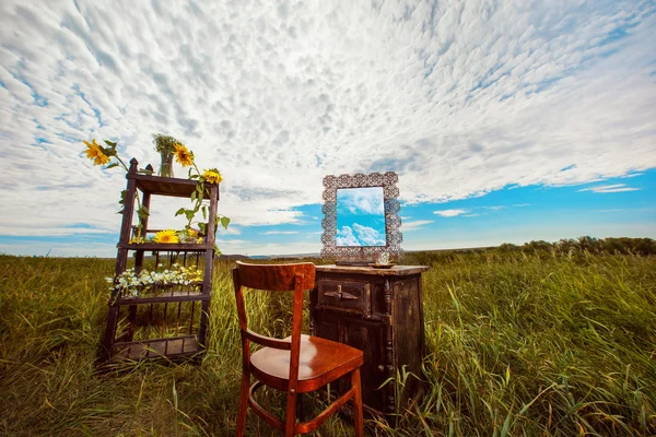 Beautiful rural landscape of field with vintage furniture decorated with wild flowers at cloudy sky summer background.