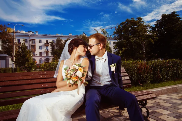 Beautiful wedding couple is kissing on bench at bright outdoors summer background.