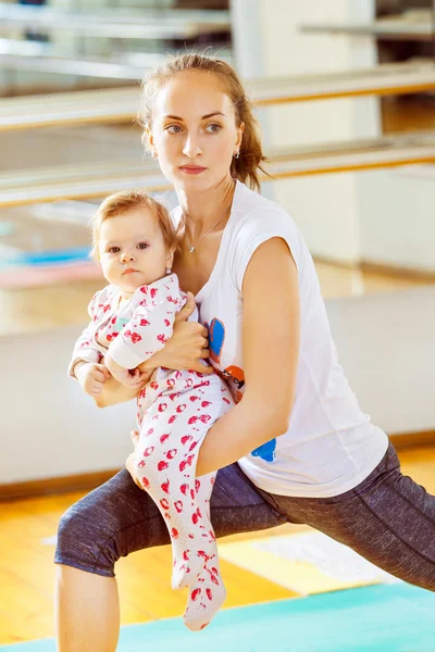Closeup portrait of mom and baby making fitness exercises at gym background.