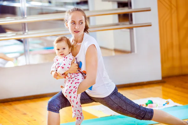 Closeup portrait of mom and baby making fitness exercises at gym background.