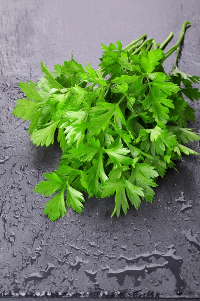 A bunch of fresh parsley with drops on black slate background.