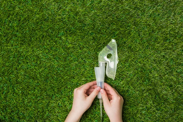 Hands holding inhaler mask over green grass.