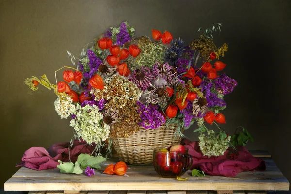 A large bouquet of dried flowers with fruits in a wicker basket on the table .