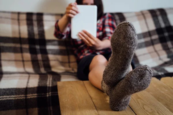 Young woman using tablet pc on couch in knitted socks