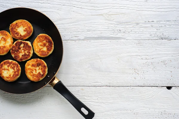 Cottage cheese pancakes in frying pan on wooden background