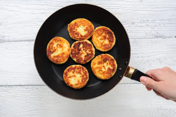Cottage cheese pancakes in frying pan on wooden background