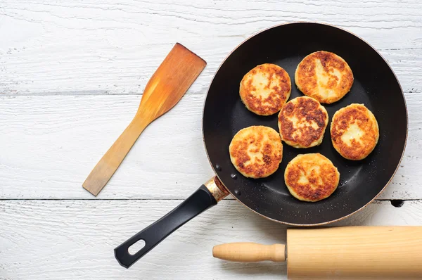 Cottage cheese pancakes in frying pan on wooden background