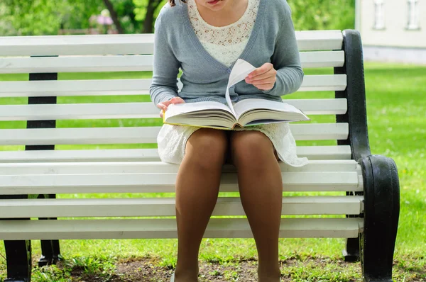 Young woman reads on a bench in park