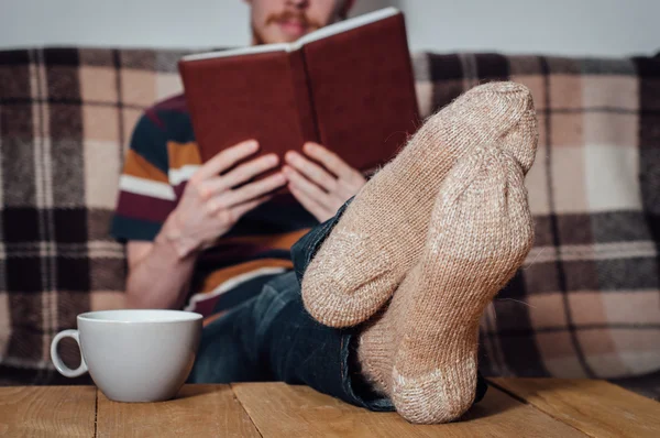 Young man reading book on couch in holey socks